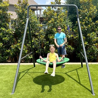 A dad pushing his daughter on a swing set.