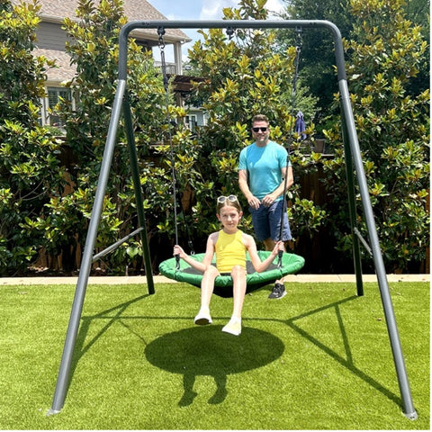 A child swinging on the gobaplay Single Swing Set while her father stands in the background.