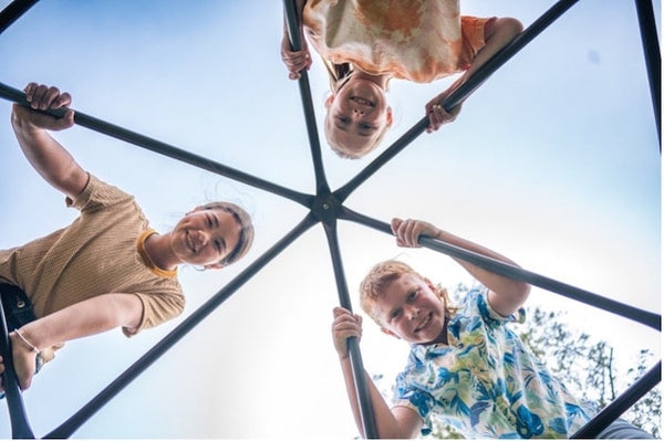 Three kids looking down from on top of a geometric climbing dome.