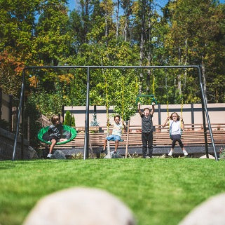 Four kids playing on a large metal swing set with multiple play features.