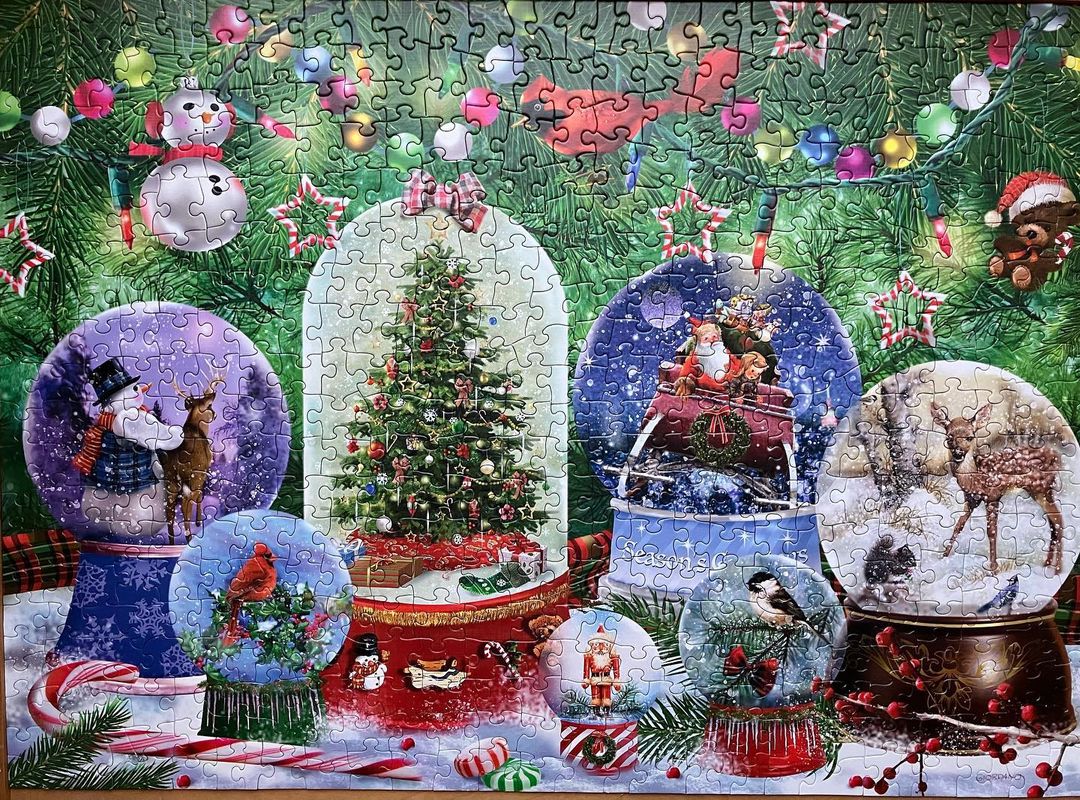 various sized snow globes on a table with wreath and lights background