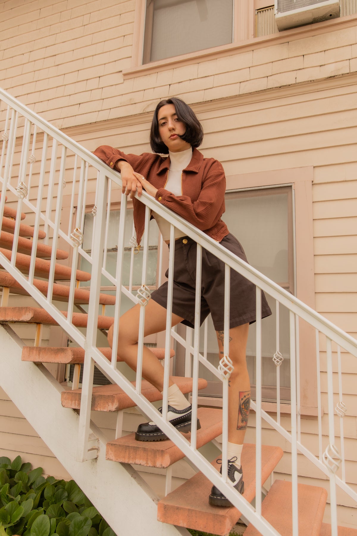 Betty is wearing Ricky Jacket in Fudgesicle Brown, Sleeveless Essential Turtleneck in Vintage Off-White, and Trouser Shorts in Espresso Brown