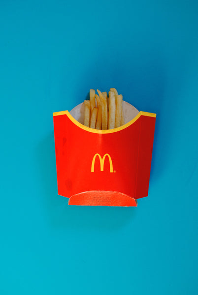 McDonald's inconic fries package with a small amount of fries in it centred on a blue table.