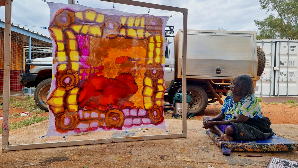 Carol Giles sitting beside a stretched silk that she hand painted