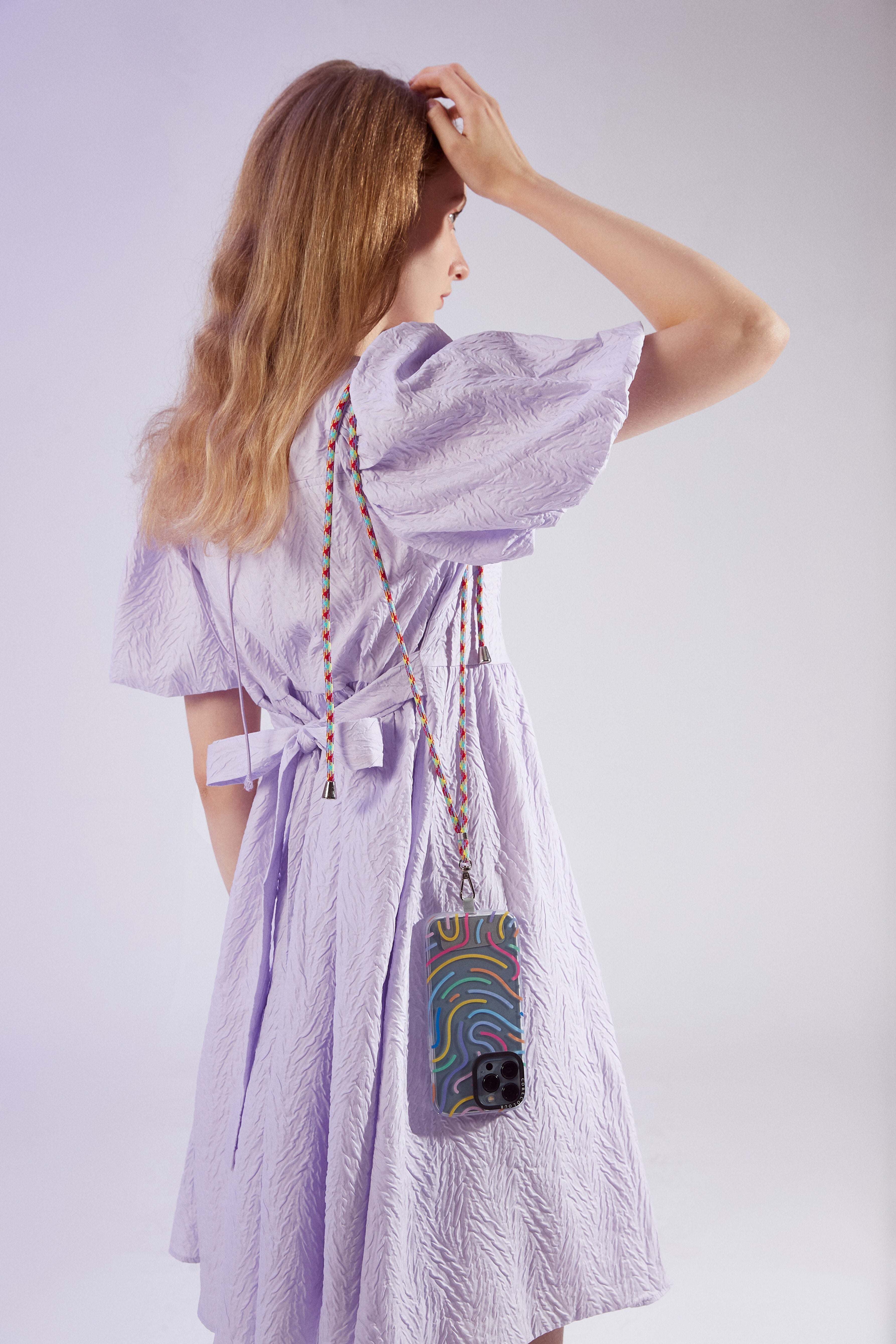 A girl in light pink dress with the stylish phone strap adorned with rainbow braided cord