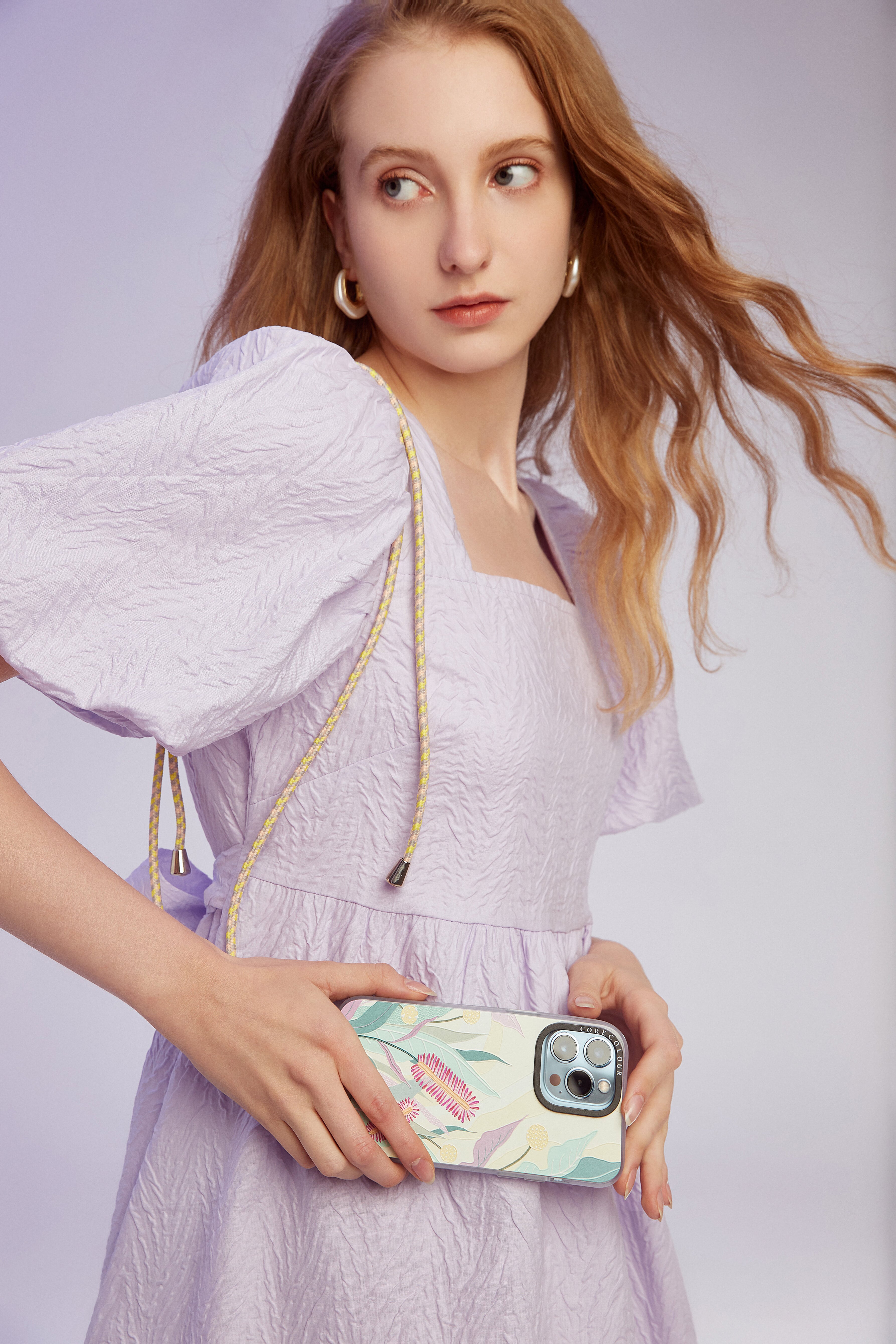 A girl in light pink dress with the stylish phone strap adorned with a yellow and white braided cord