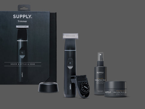 Electric beard trimmer with attachments and grooming products on a dark background.