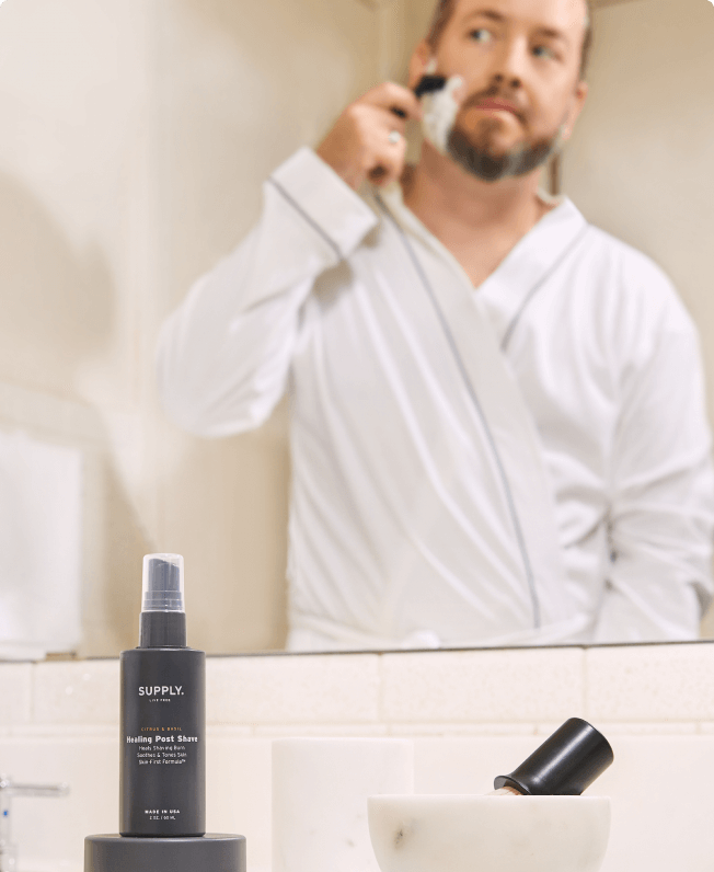 Man shaving in a bathroom, with shaving products on the counter.