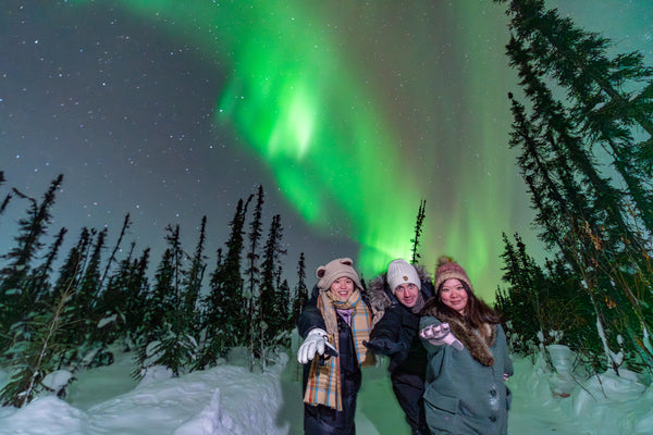 Smiling tour guests on an aurora borealis adventure in Fairbanks, Alaska in the winter with snowy trees