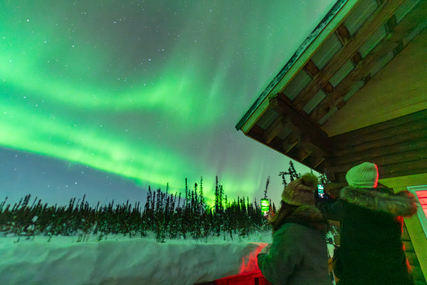 Tour guests looking at a bright aurora in the winter wilderness near Fairbanks, Alaska