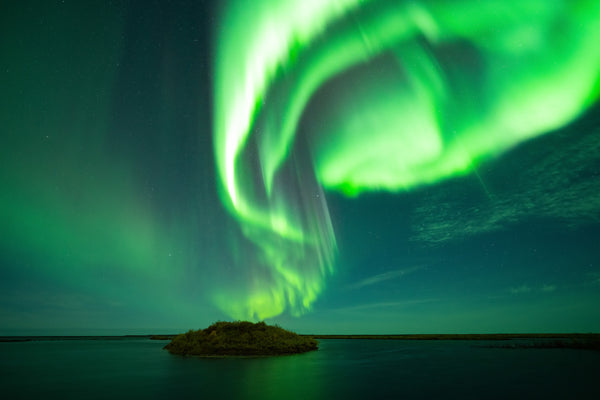 The aurora borealis swirling above an island in a lake in northern Canada captured by Vincent Ledvina.