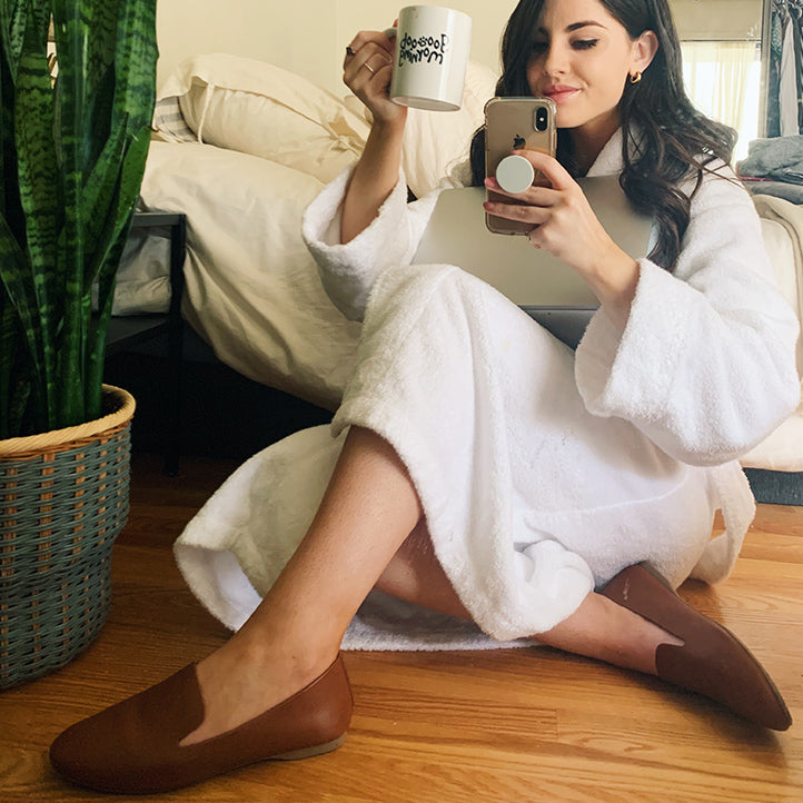 Girl holding coffee mug and wearing a robe with Birdies Starling flats in cognac leather