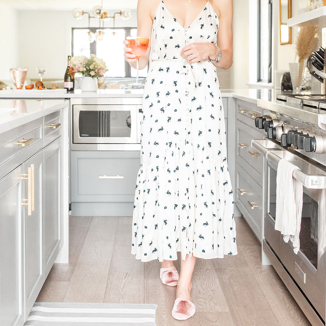 Sophie walking with her rosé spritz while wearing a flower dress and Songbird slides in light pink