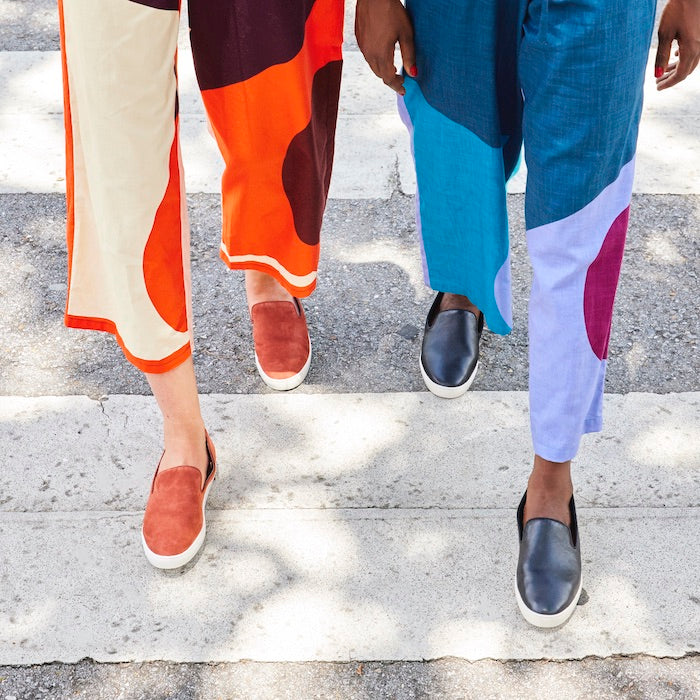 two women wearing slip-on sneakers and colorful jumpsuits