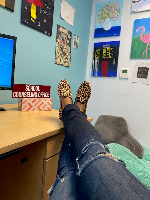 woman wearing cheetah flats with feet up on desk