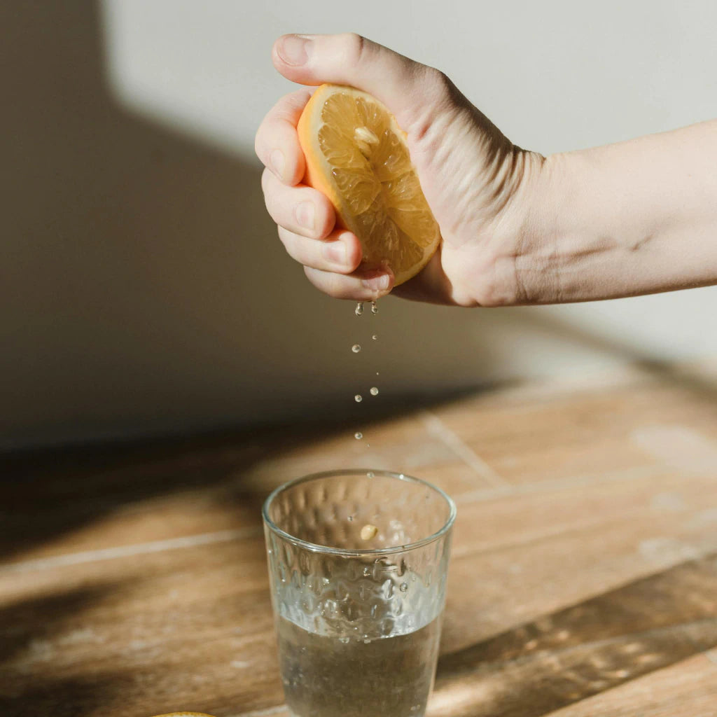 Eine Hand, die eine halbe Zitrone über einem Glas auspresst