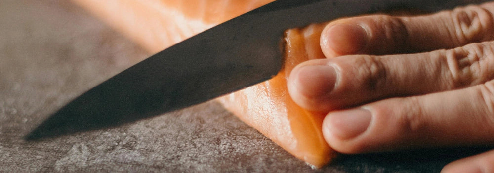 Eine Hand, die mit einem Messer ein Stück Lachs zerteilt