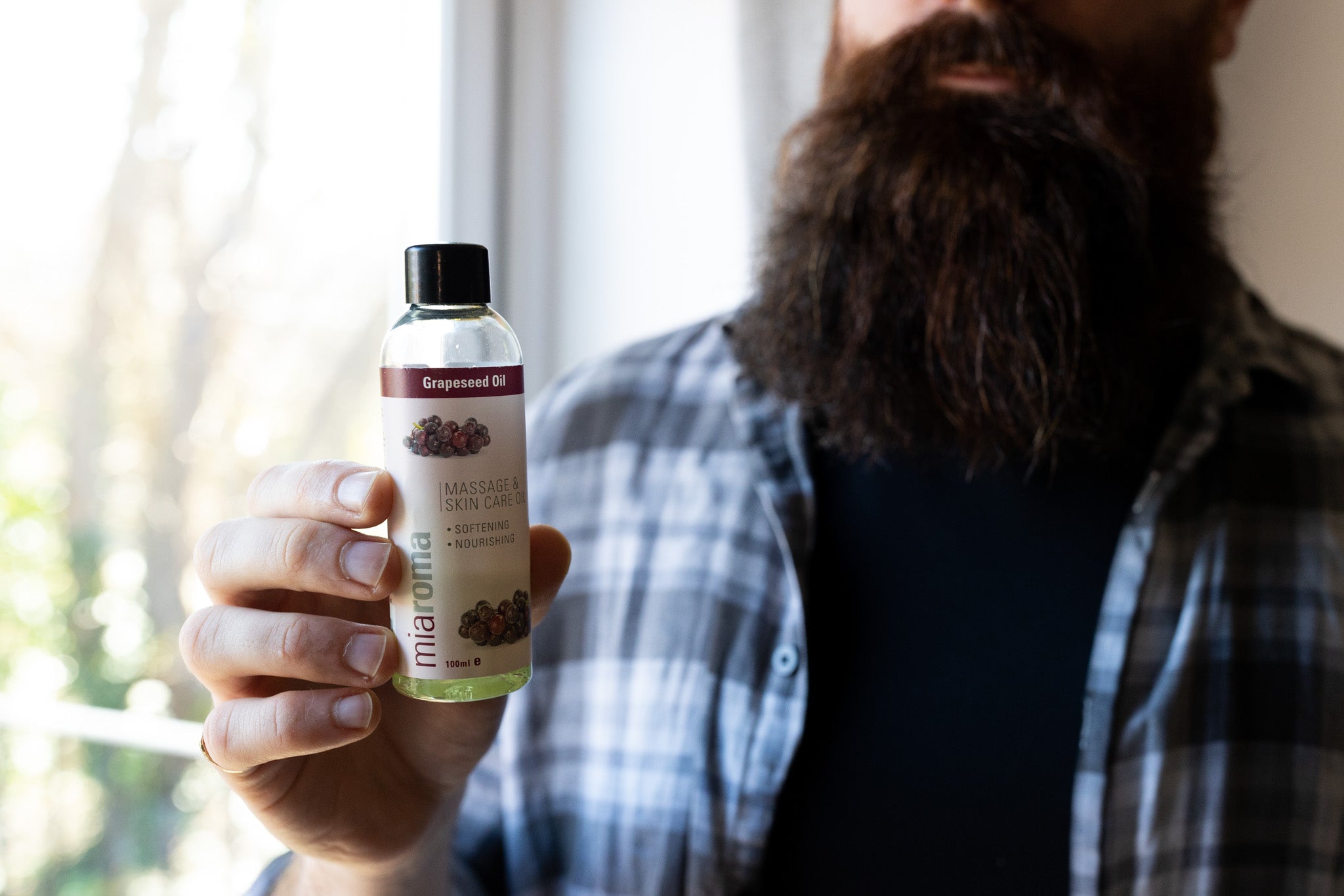 Alex, owner of Mission Beard, holding an unscented grapeseed oil for beard care