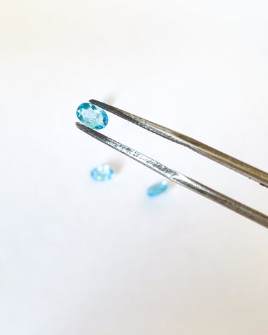 A beautiful unset oval swiss blue topaz held with tweezers with other topaz in the background