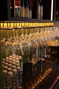 Wine glasses hanging upside down above corked wine bottles on a bar.