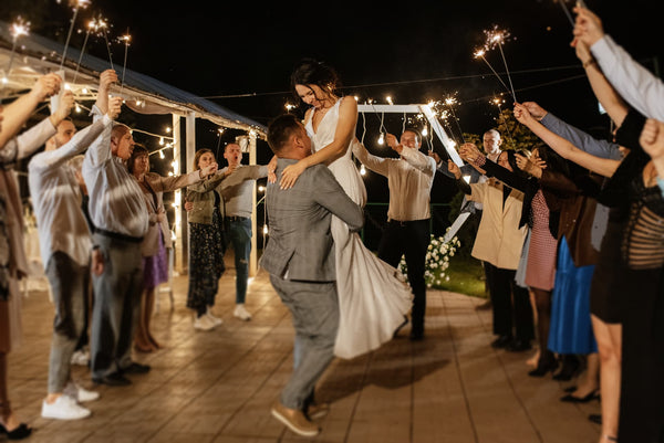 groom lifting his bride with people around them holding sparklers