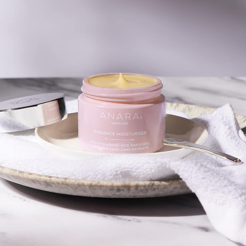 Anara Radiance Moisturiser with lid off showing the texture on a white towel and sitting on a plate.