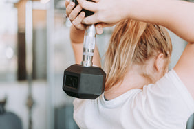 Eine Frau hebt beim Sport eine Hantel hinter ihren Kopf