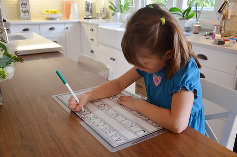 child writing on a placemat at the dinner table