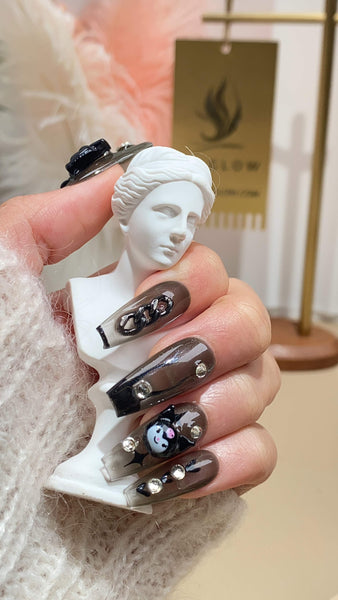 Hand holding a white miniature bust of a woman, showcasing detailed press-on nails with artistic designs against a blurred background featuring the LTGlow logo.