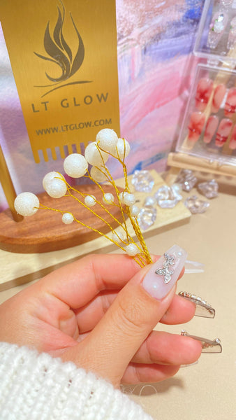 A hand showcasing elegant press-on nails with a white and crystal design, holding a decorative branch, with the golden LT GLOW brand card and a selection of nail designs in the background