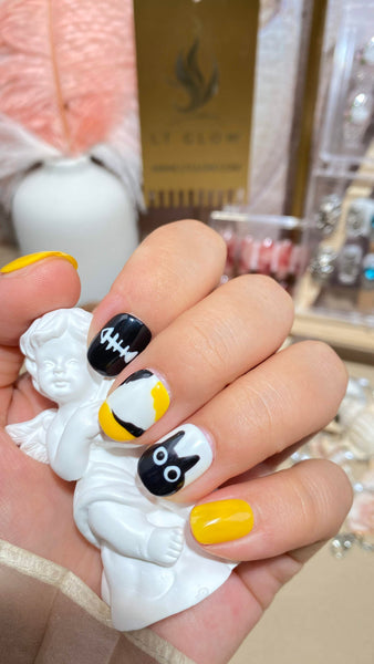 Hand displaying acrylic nail designs with unique patterns, including a penguin and football motif, against a backdrop featuring an "LT Glow" sign and decorative elements