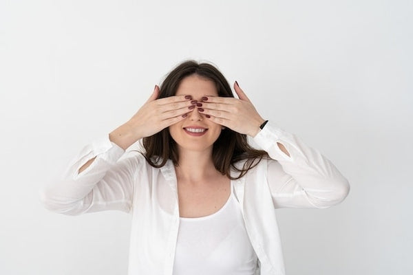 Woman with false nails playfully covering her eyes against a white background