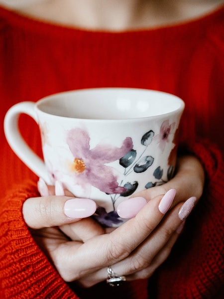 Woman holding a floral mug showcasing delicate pink handmade false nails against a red sweater background