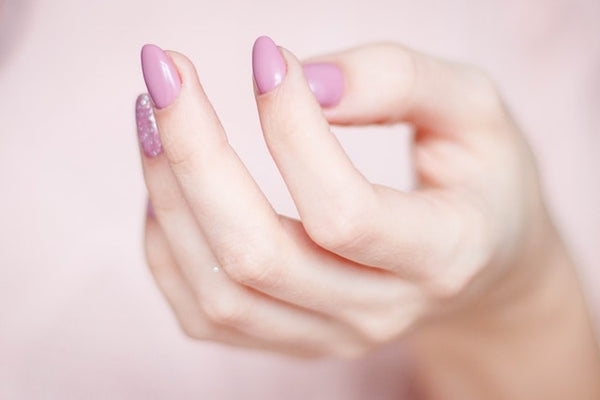 The nails are adorned with handmade fake nails in a delicate shade of pink, with one nail featuring a sparkling glitter accent. The image exudes elegance and sophistication