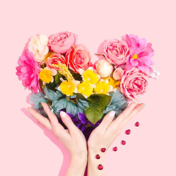 Elegant hands showcasing handmade fake nails while cradling a vibrant bouquet of flowers against a soft pink background