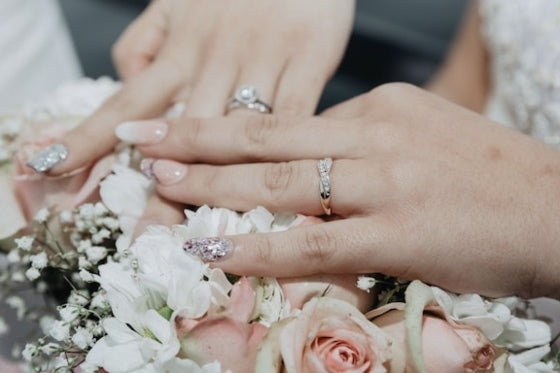 Bridal hands adorned with sparkling handcraft fake nails, elegantly placed over a bouquet of roses and white flowers