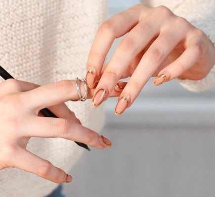 Two hands with golden handcrafted false nails being adjusted, highlighting elegant nail art and fashionable rings