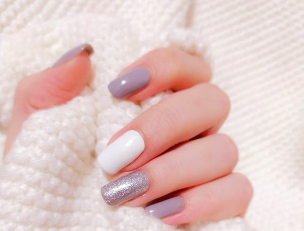 Close-up of hand showcasing handcrafted press-on nails in a cozy white textured fabric, featuring a combination of glossy white, matte lilac, and glittery silver finishes