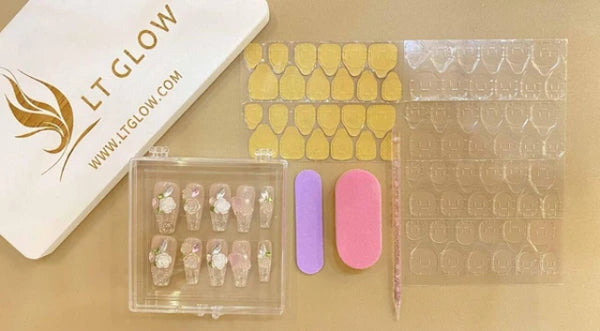 A set of handcrafted false nails displayed in a clear box, accompanied by adhesive tabs, nail buffers, and branding from LTGLOW