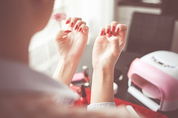 A person admires their freshly painted acrylic nails, holding them up against a backdrop of nail polish bottles and a nail lamp on a salon table