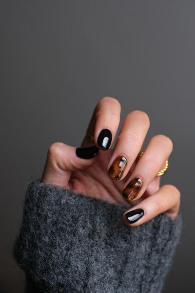 Elegant hand showcasing a set of false nails with black and amber marbled designs, complemented by a cozy grey sweater