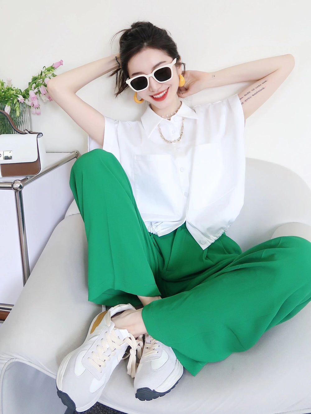 An alluring woman in a white shirt and green pants, epitomizing grace and style with her Korean fashion sunglasses.
