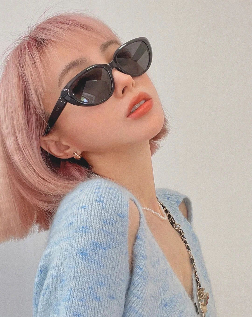 Witness the embodiment of glamour! Adorned with stunning pink hair, this fashionable woman exudes an air of sophistication, accentuated by her trendy sunglasses.