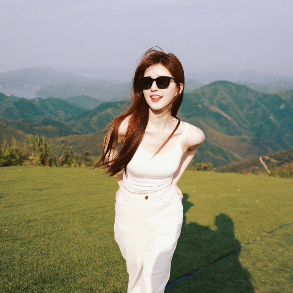 A stylish woman, donning white pants and chic sunglasses, gracefully stands atop a majestic mountain, exuding an air of elegance and adventure.