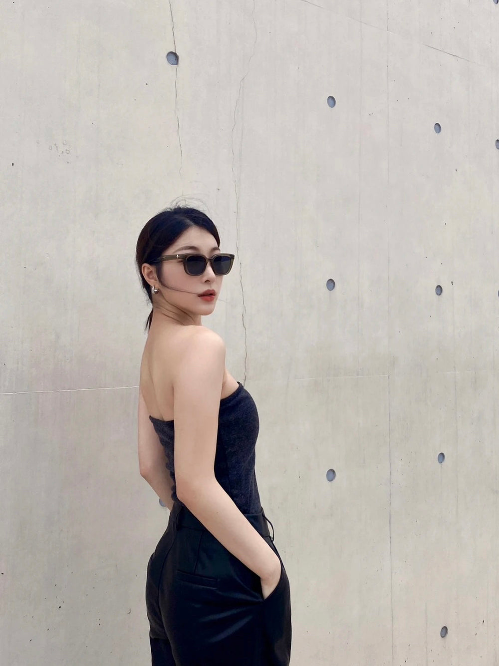 A captivating woman exudes elegance in her sleek black dress, complemented by stylish sunglasses. She exudes an air of mystery and sophistication. 