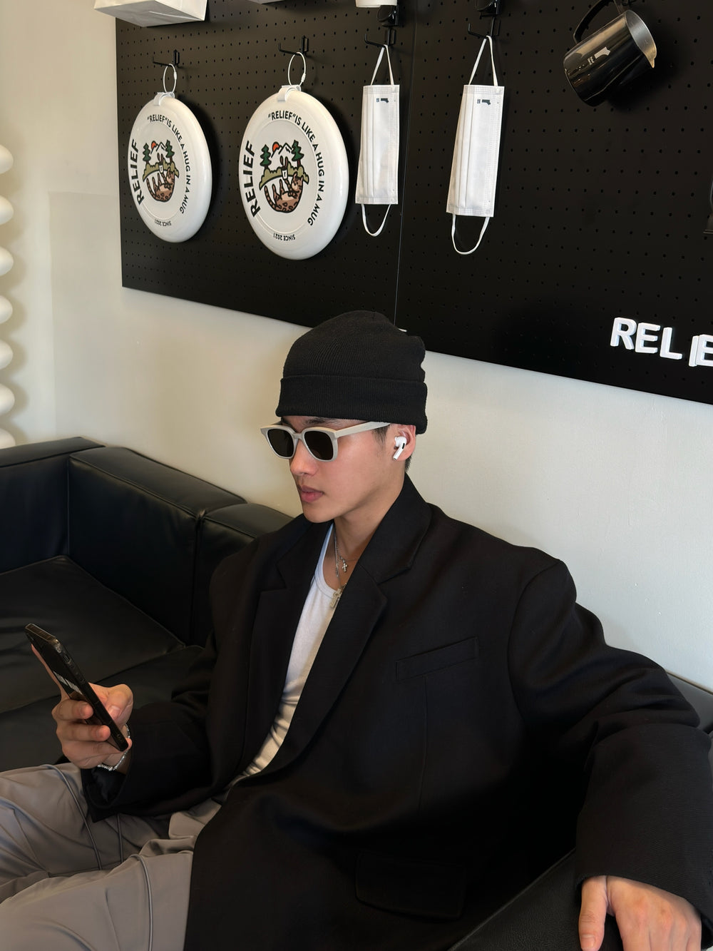 A man with a sleek look, wearing stylish sunglasses and a black jacket, relaxing on a couch.