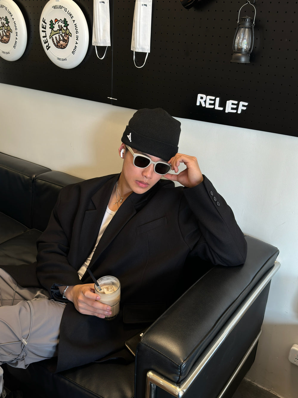 A person in a black jacket and hat, enjoying a seat on a couch wearing his luxury sunglasses.