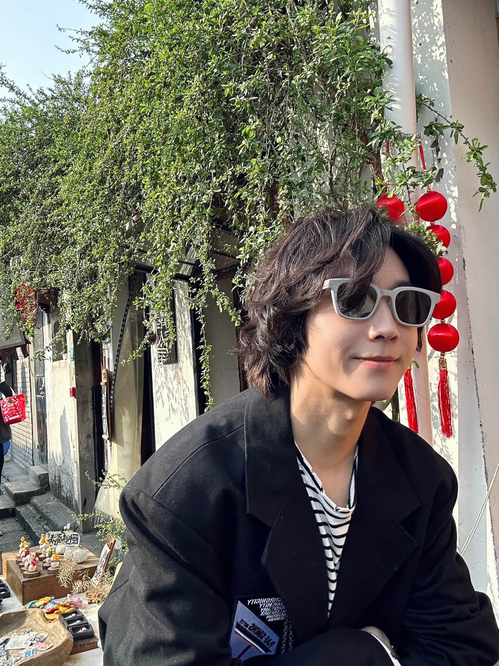 A dapper gentleman, donned in a sleek black jacket and stylish sunglasses, exudes an air of sophistication while leisurely seated on a bench.