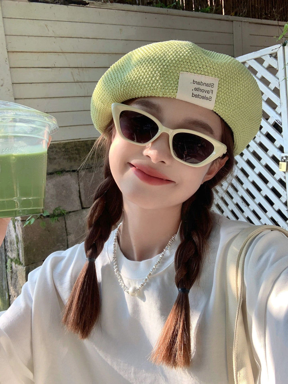 Behold the epitome of health and style! A chic woman donning sunglasses and a hat, sipping on a refreshing green smoothie. 