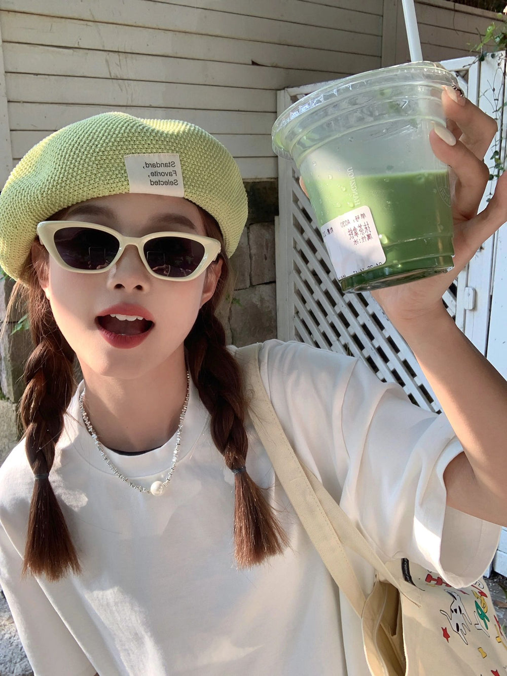 With an air of elegance, a woman sporting a fashionable hat and stylish sunglasses gracefully holds a cup of invigorating green juice, embodying both sophistication and a commitment to well-being.